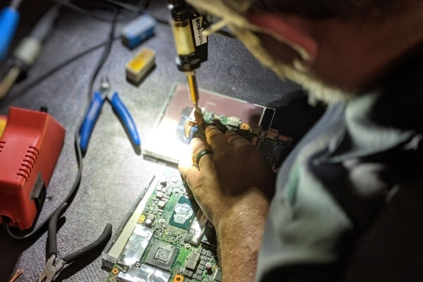 Man using a tool to repair a computer motherboard
