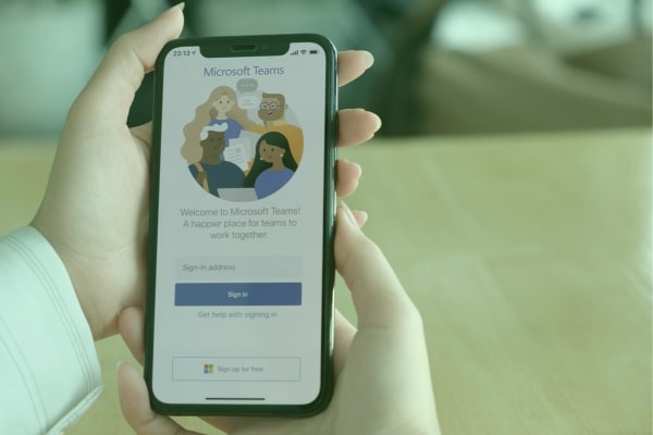 Hands holding a cell phone with the Microsoft Teams login on the screen